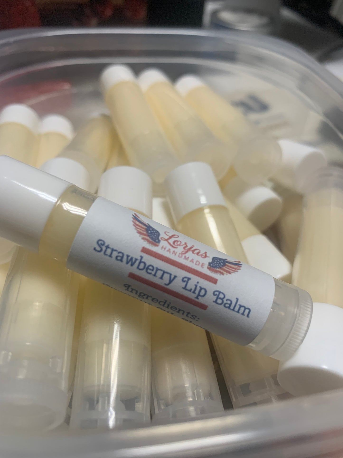 Strawberry lip balm with a LorJas Handmade brand label in a plastic container.