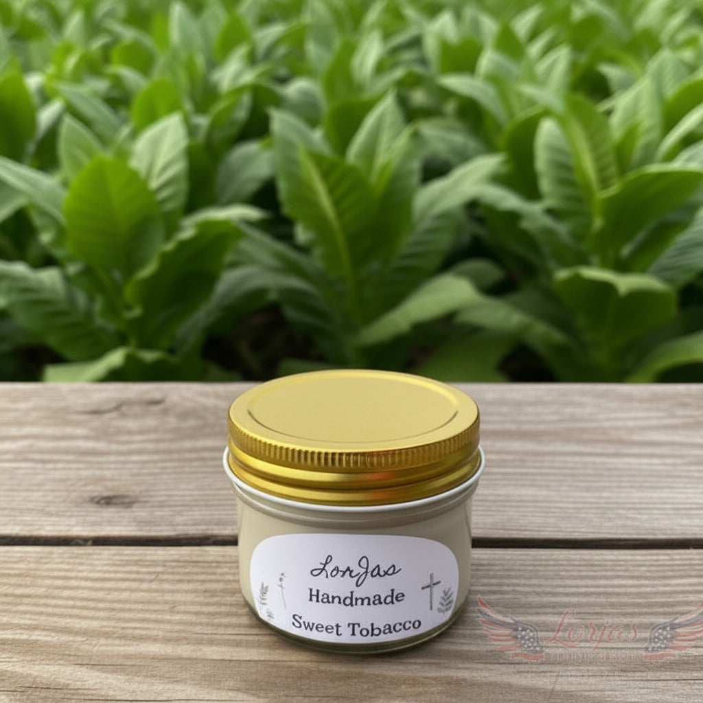 LorJas Handmade Sweet Tobacco lighly scented soy candle on a wooden surface with green farm grown plants as a backdrop featuring LorJas Handmade brand logo