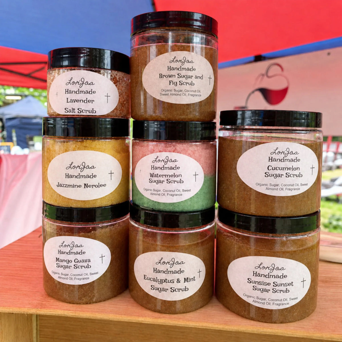 Collection of handmade sugar scrubs in jars with visible labels on a wooden shelf.
