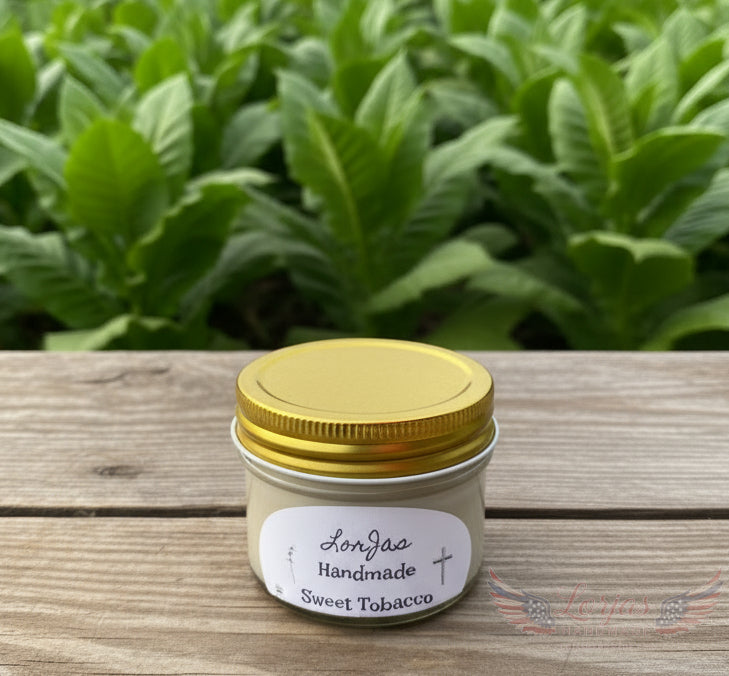 Jar with gold lid and 'LorJas Handmade Sweet Tobacco' label on a wooden surface with green leaves in the background