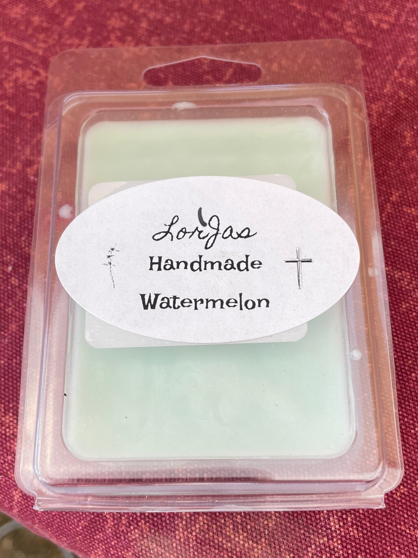 Packaged wax melt labeled 'LorJas Handmade Watermelon' on a red textured surface.