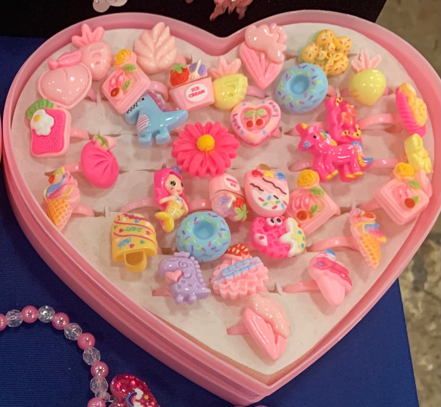 Heart-shaped display filled with colorful acrylic caricature-shaped jewelry on a blue tablecloth