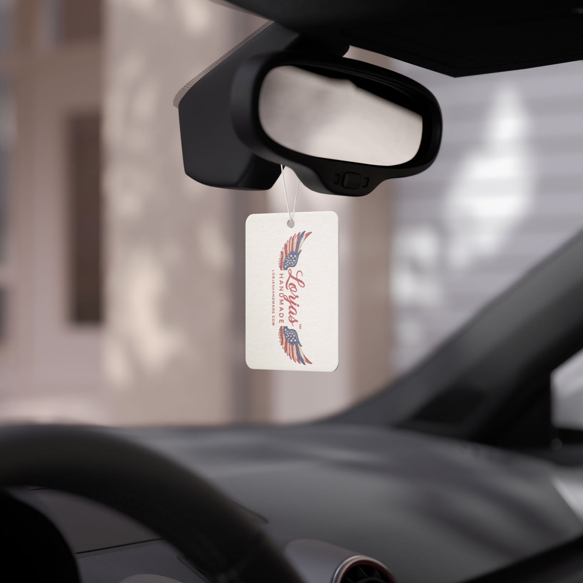 LorJas Handmade branded car air freshener hanging from a car's rearview mirror with a blurred background.