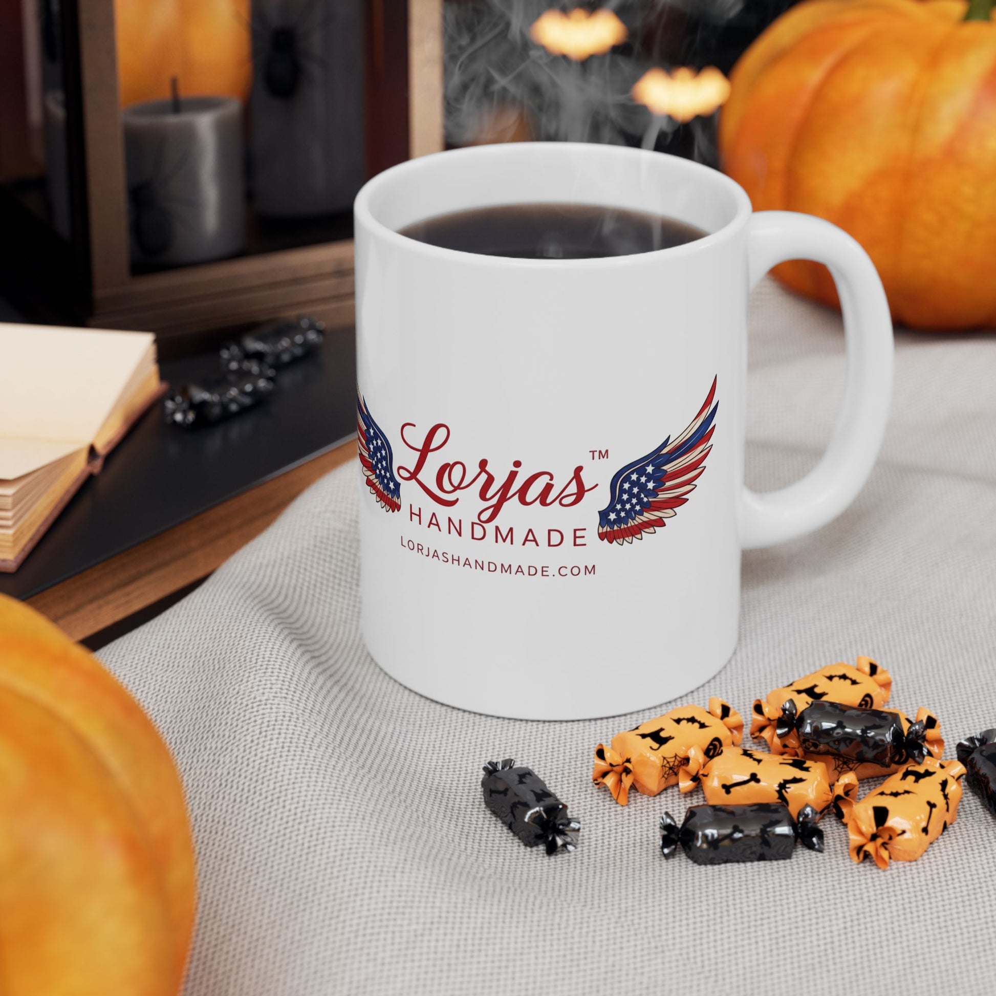 White mug with 'Lorjas Handmade' logo on a table with Halloween-themed treats and pumpkins.