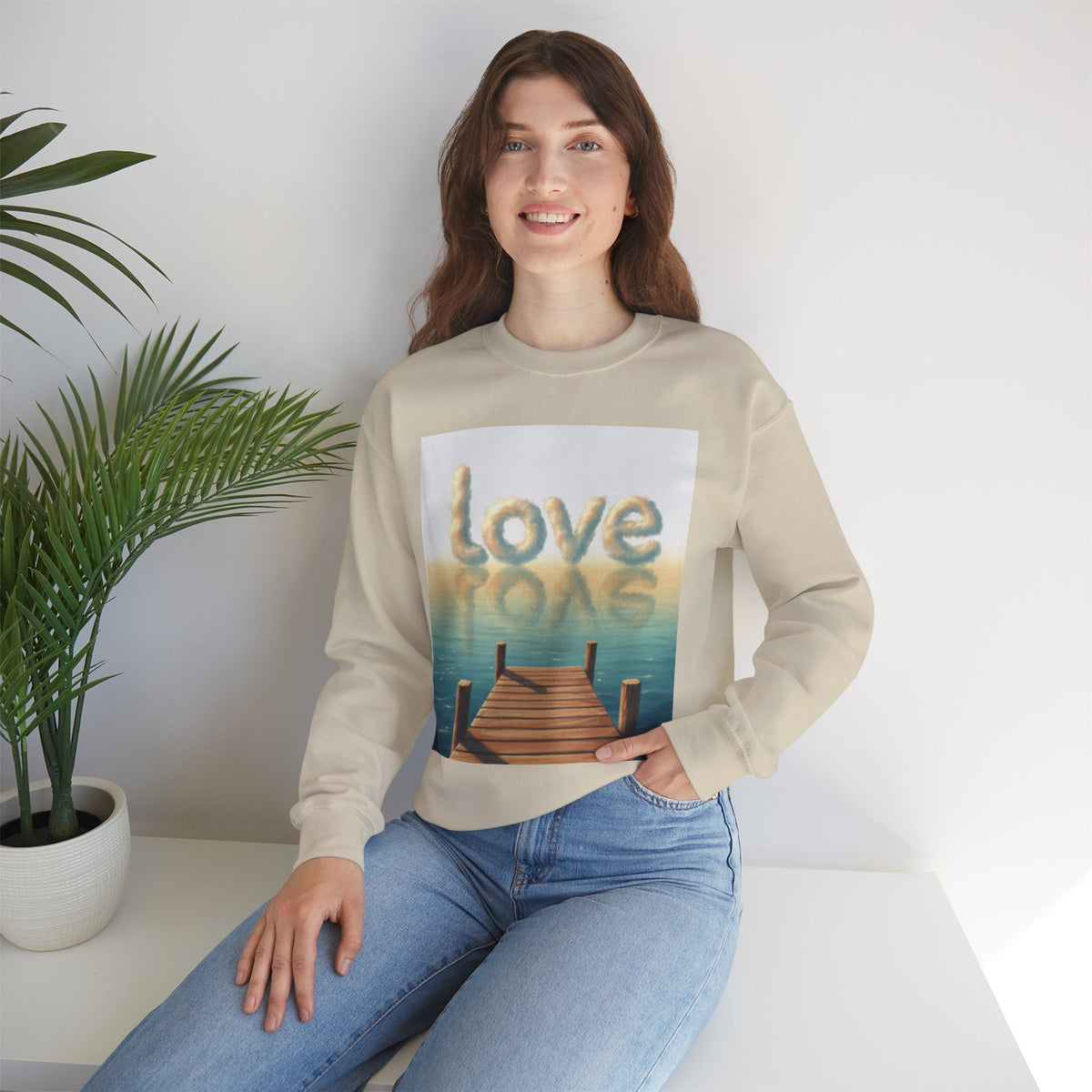 Woman wearing a beige sweatshirt with a graphic design sitting on a white surface.