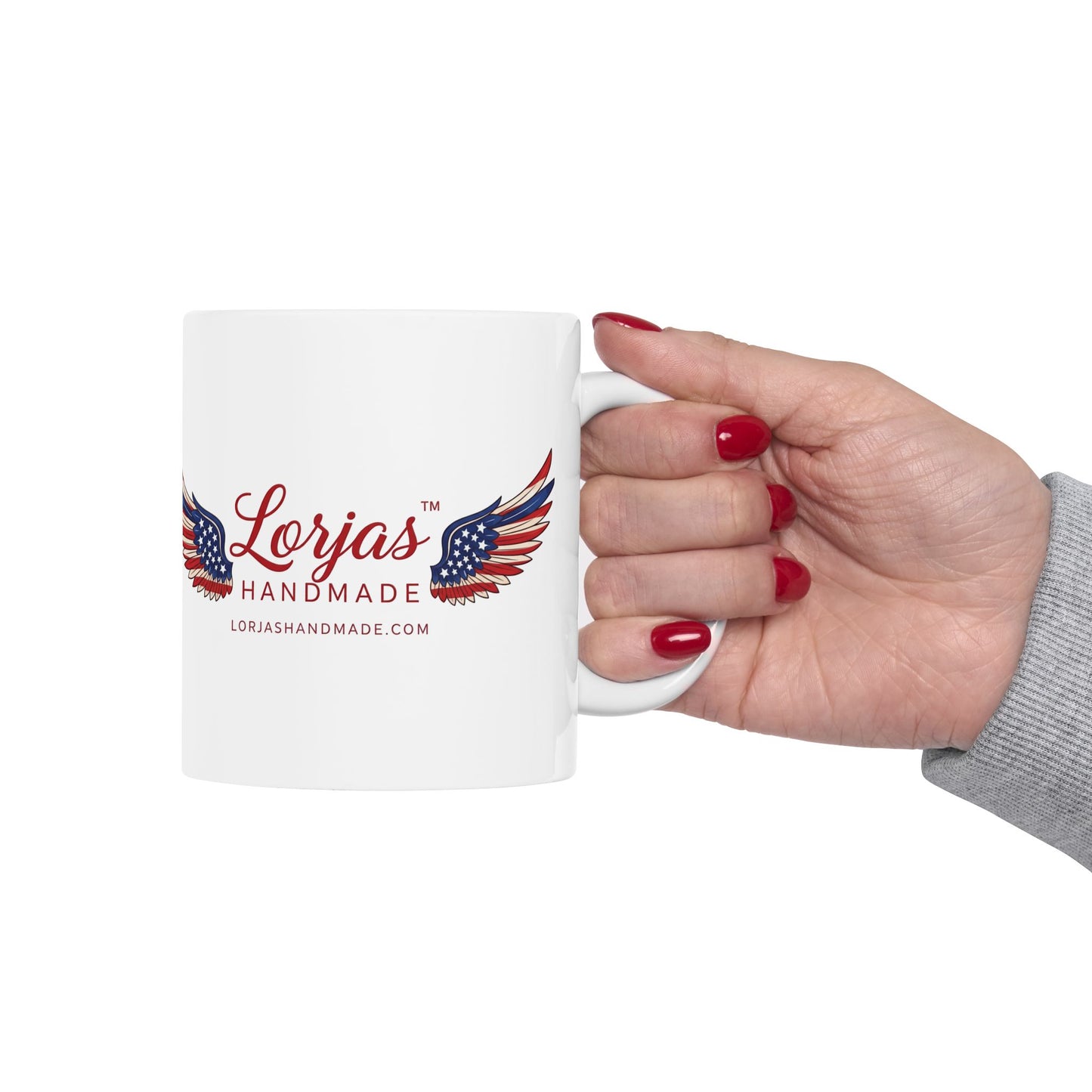 Hand holding a white mug with 'Lorjas Handmade' logo on a white background