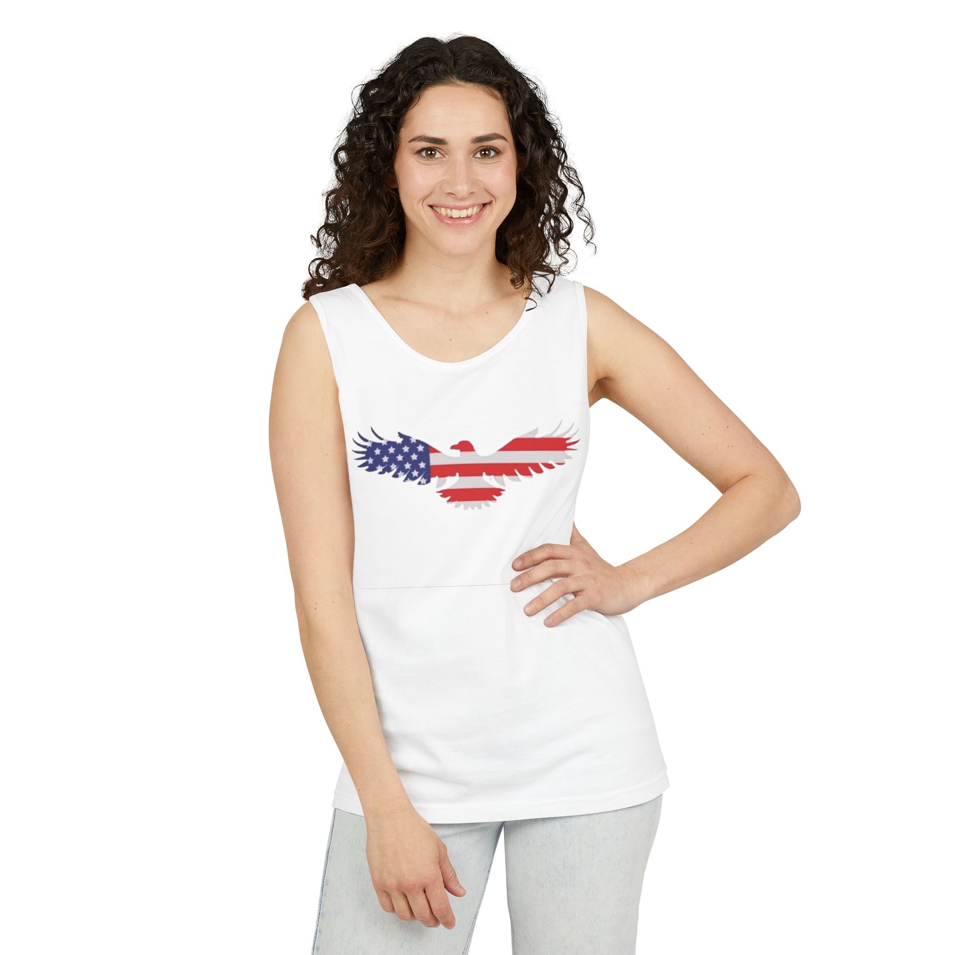 A woman modeling a white sleeveless tank top with a distressed eagle graphic filled with the American flag pattern, paired with light gray pants, against a plain white background.