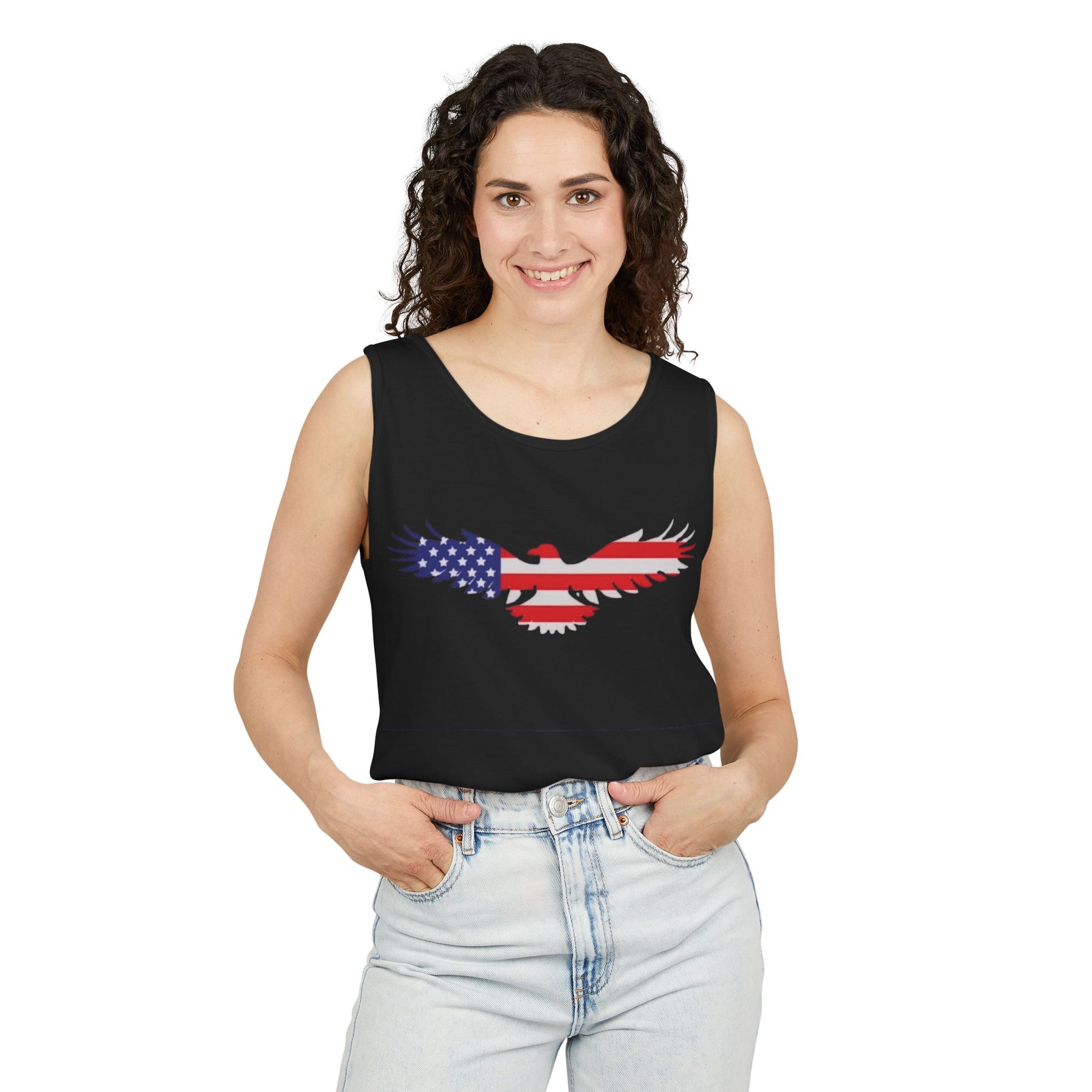 A woman modeling a black sleeveless crop top with a graphic of an eagle filled with the American flag pattern, paired with light-wash jeans against a plain white background.