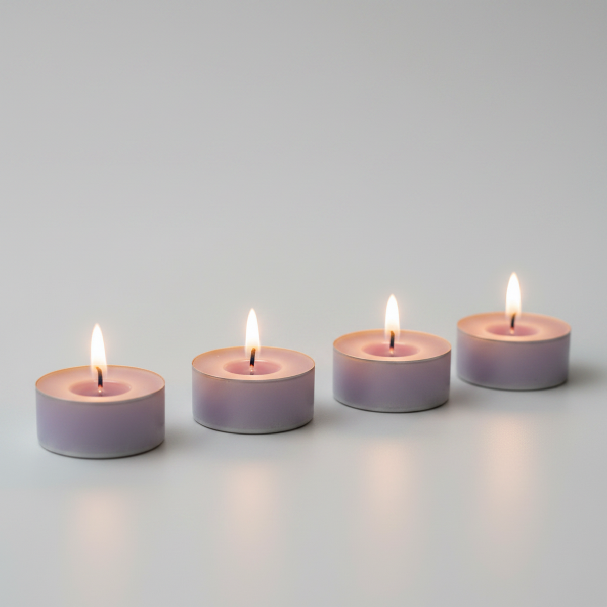 Four lit light purple LorJas Handmade lightly scented soy tealights with a gray studio background.