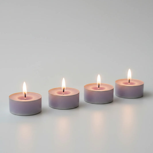 Four lit light purple LorJas Handmade lightly scented soy tealights with a gray studio background.