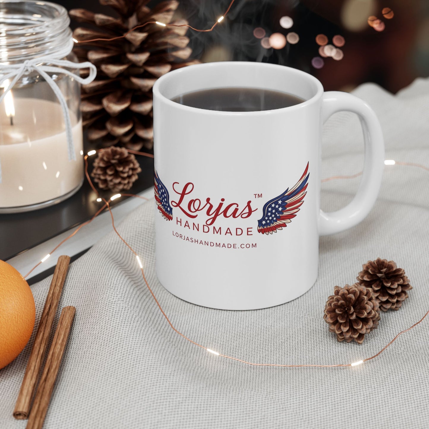 White mug with 'Lorjas Handmade' logo on a table with decorative items
