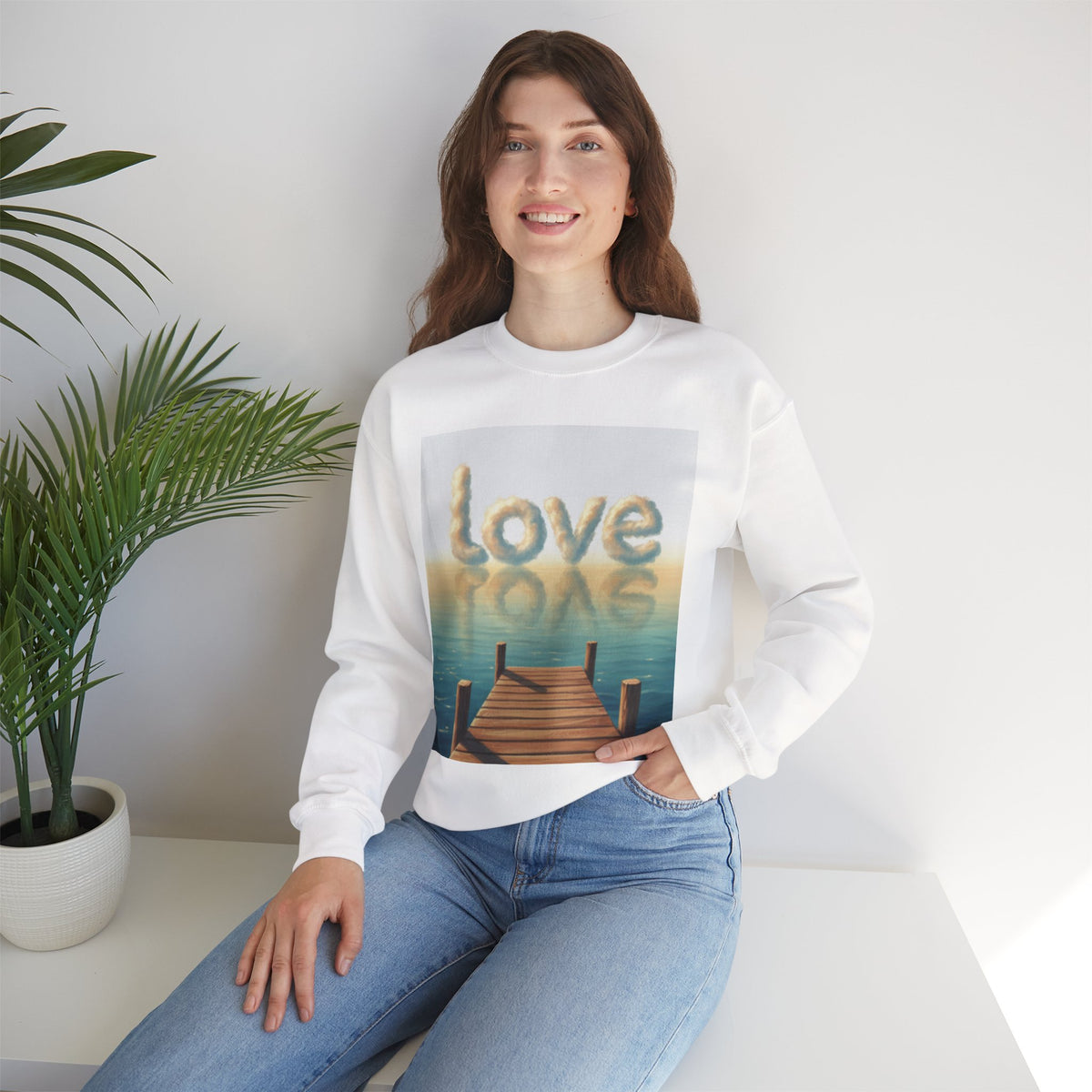 Woman wearing a white sweatshirt with a 'Love is Love' graphic, sitting in a room with a plant.