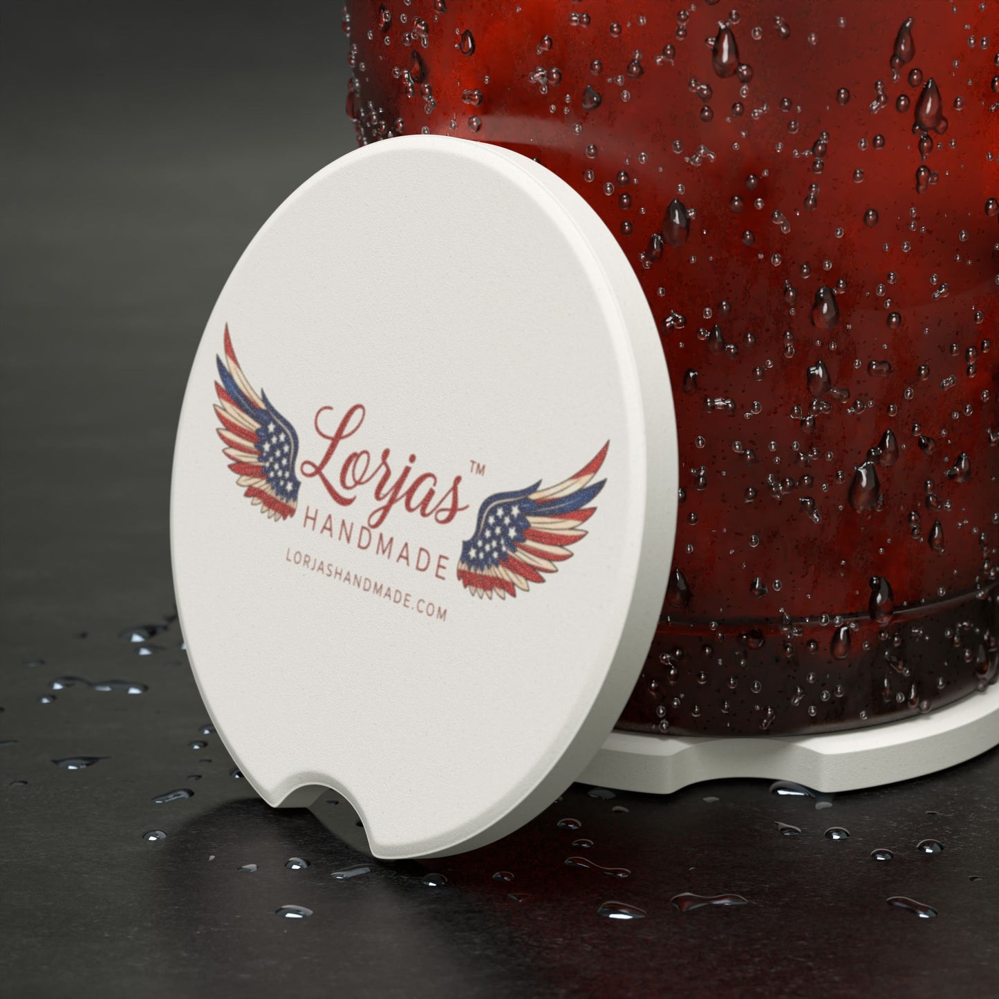 White coaster with 'Lorjas Handmade' logo on a dark surface with a red container.