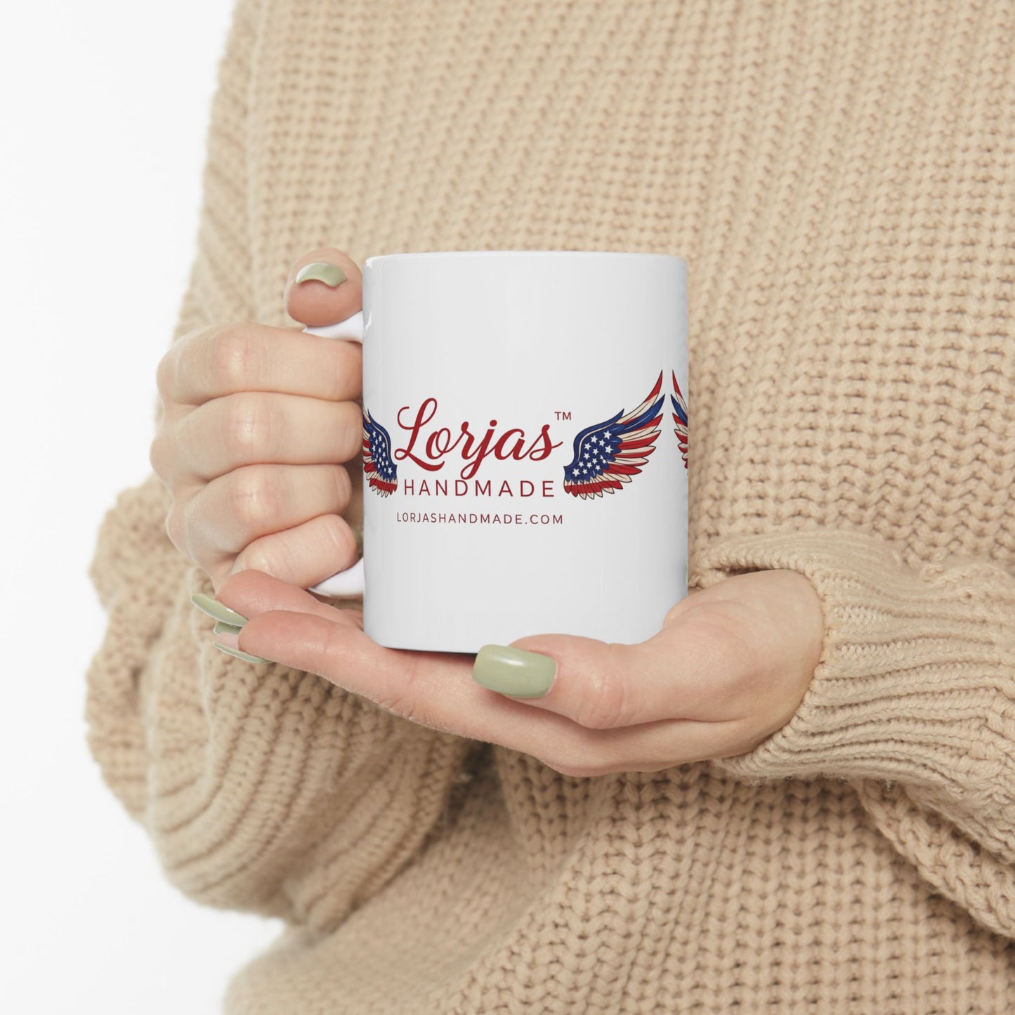 Person holding a white mug with 'Lorjas Handmade' logo, wearing a beige sweater.