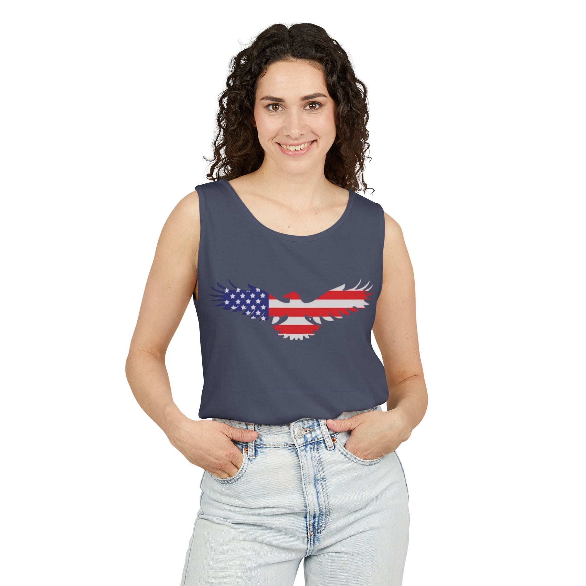 A woman modeling a navy blue sleeveless tank top with a graphic of an eagle filled with the American flag pattern, paired with light-wash jeans against a plain white background.