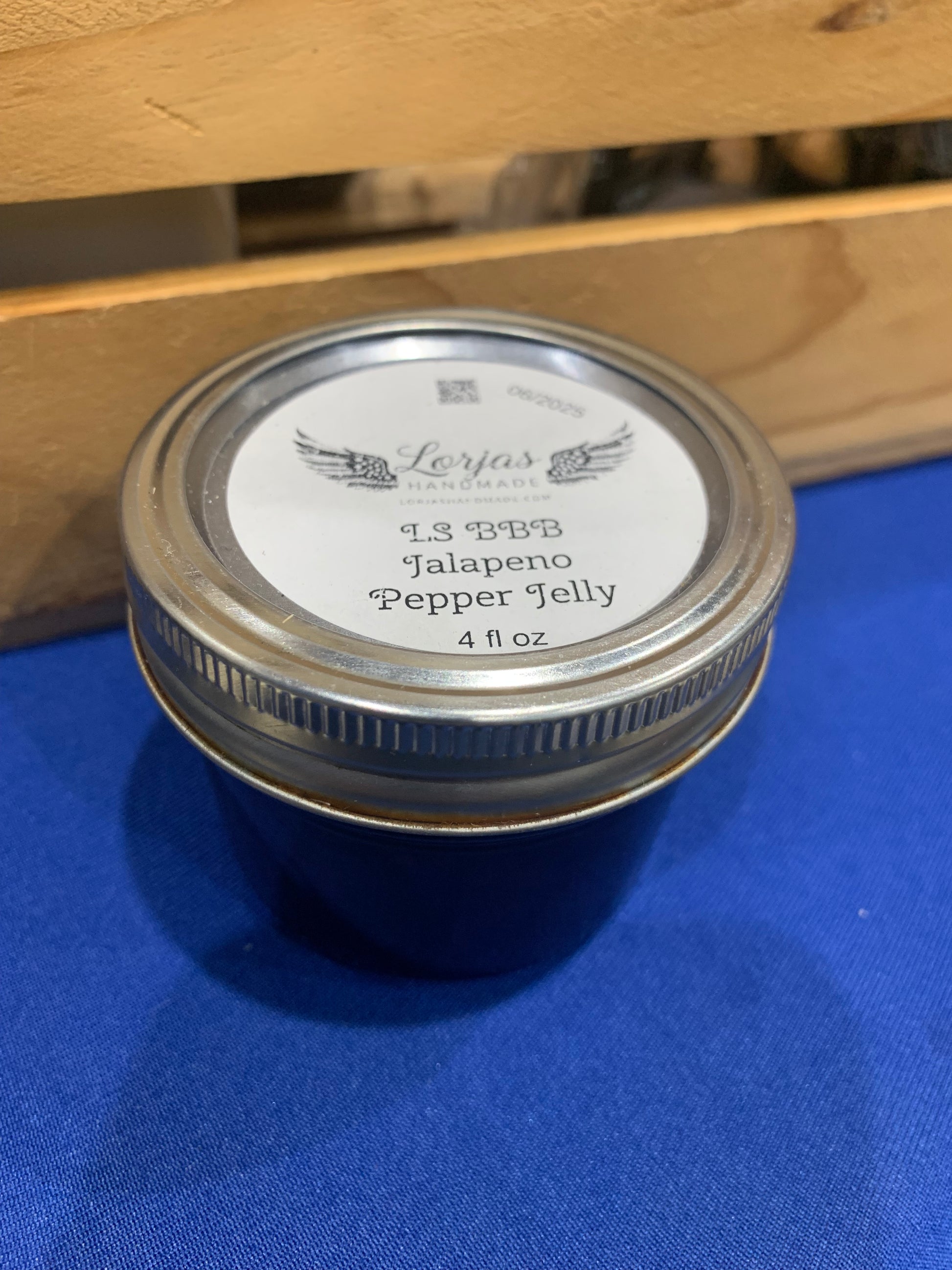 Jar of LorJas Handmade 'BBB Jalapeño' pepper jelly with a label on a blue surface with wooden background