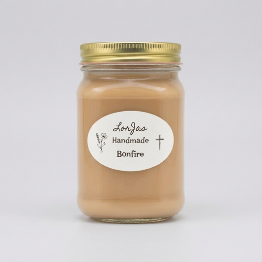 A glass jar candle filled with a light tan wax, sealed with a gold metal lid and featuring a white oval label that reads 'Lor'Jas Handmade Bonfire' with a light grey studio background.