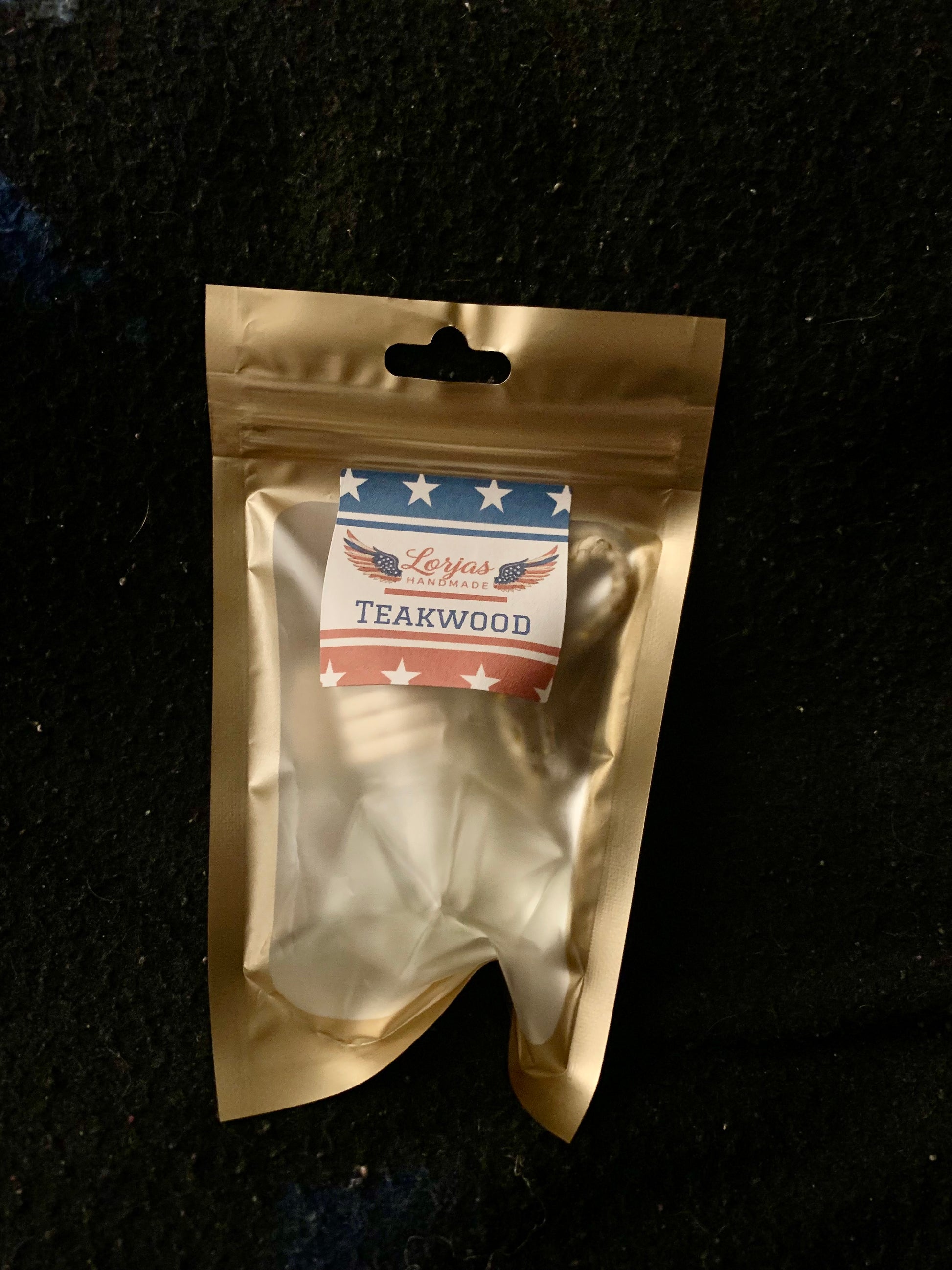 Gold packaging of Teakwood car diffuser with a LorJas Handmade label on a black background