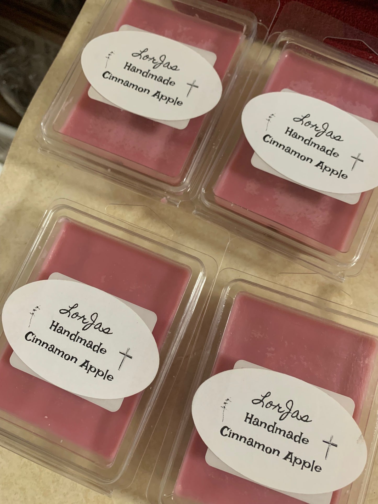 Four pink LorJas Handmade 'Cinnamon Apple' scented organic soy wax melts in clear packaging with labels on a beige surface.
