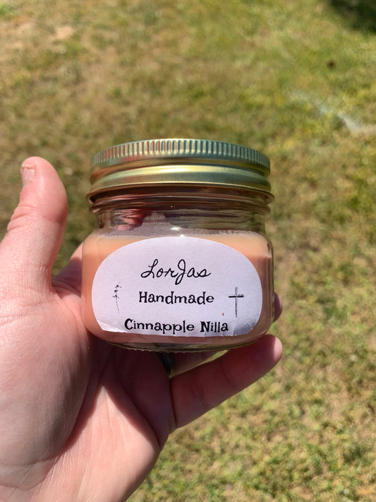 LorJas Handmade 'Cinnapple Nilla' scented candle held in hand with a label against a grassy background