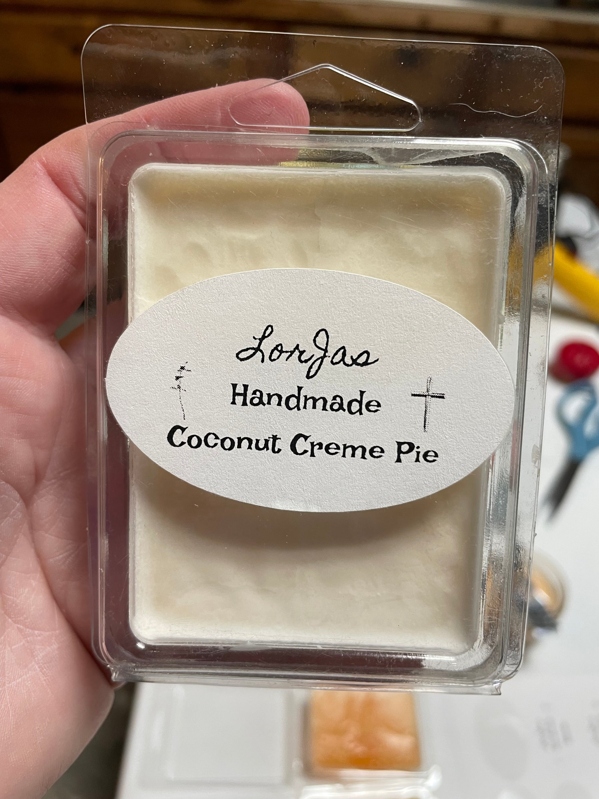 LorJas Handmade 'Coconut Creme Pie' scented wax melt being held in a hand with a blurry background