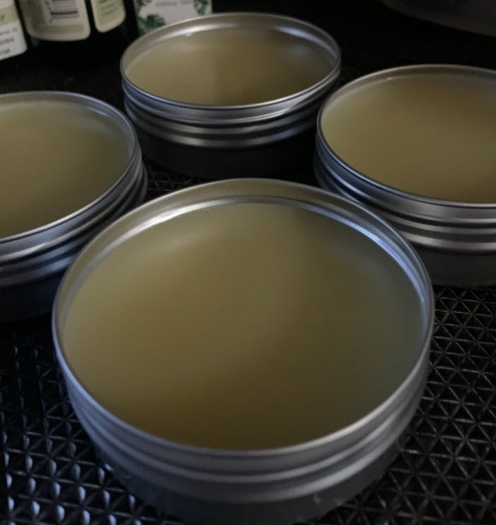 Stacks of metal tins filled with LJH beard balm in the process of curing on a textured tabletop.