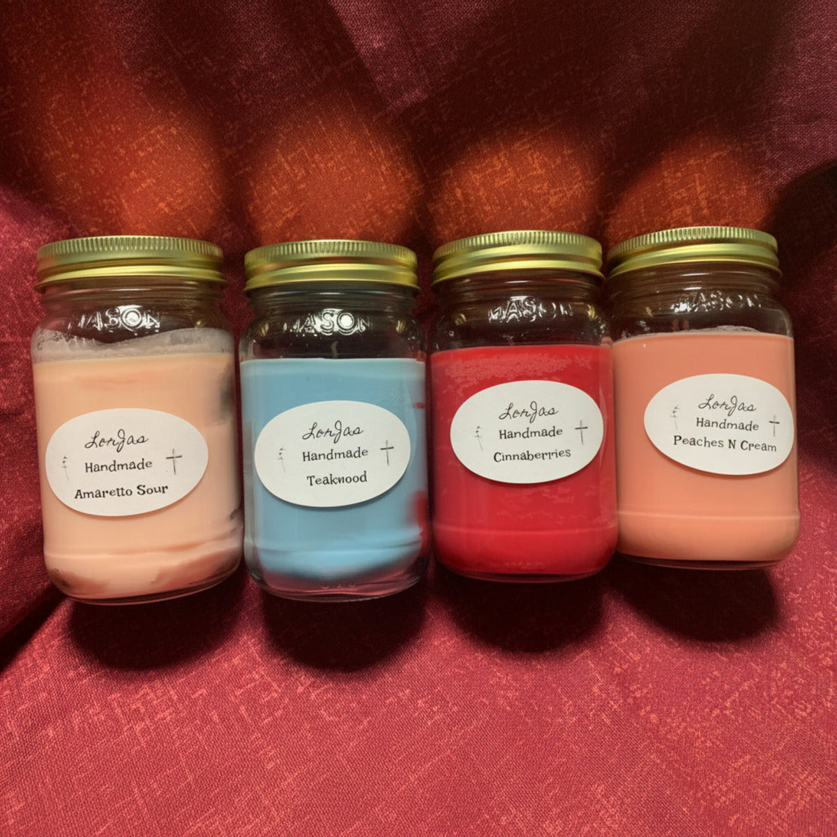 An in-process order of four 16 ounce jars of LorJas Handmade soy lightly scented candles with brand labels on a red textured surface.