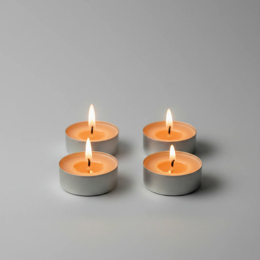 Four lit tealight candles in small silver metal holders arranged in a 2x2 grid on a smooth light gray surface with a soft gray background.