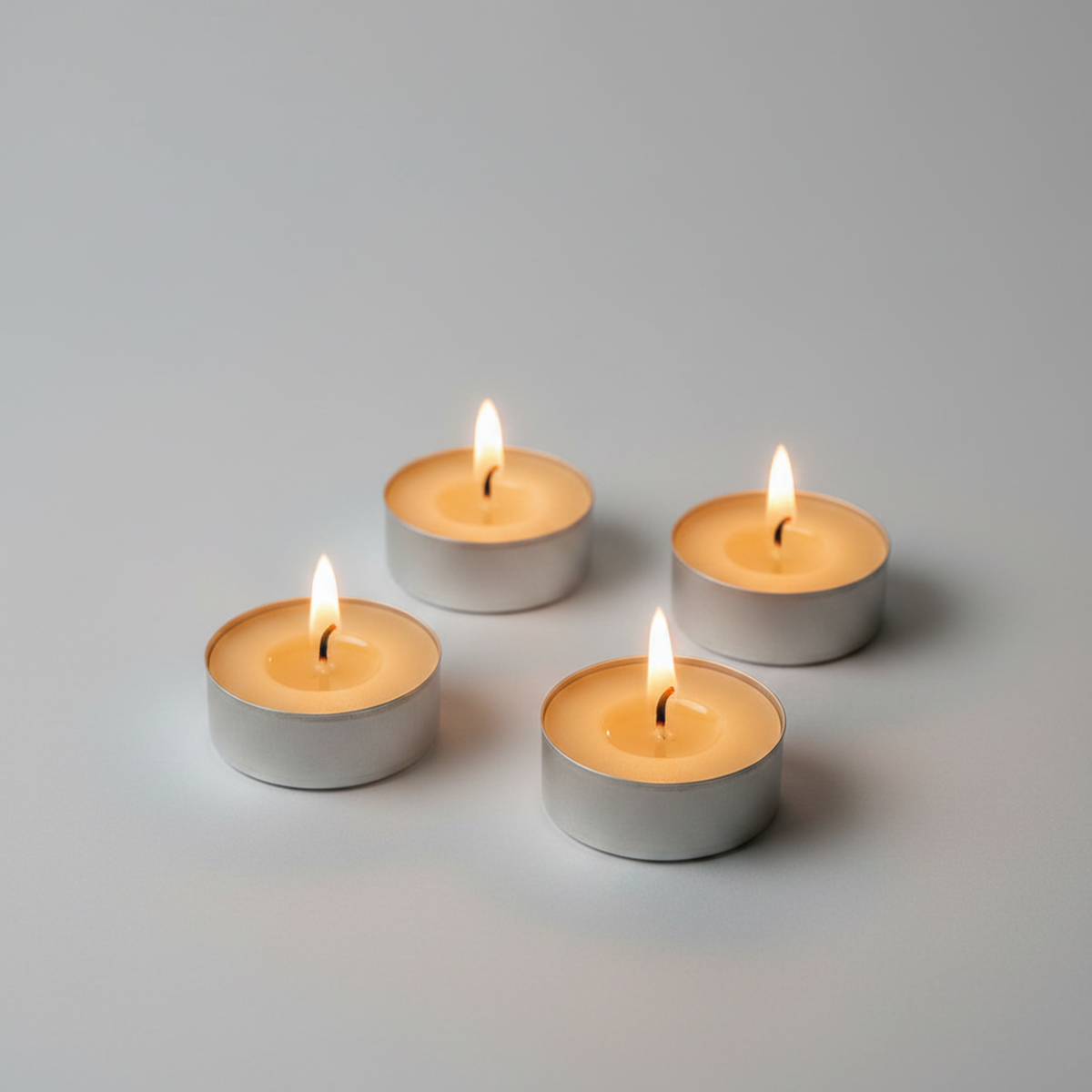 Four lit silver tea light candles arranged in a square on a clean light gray background.