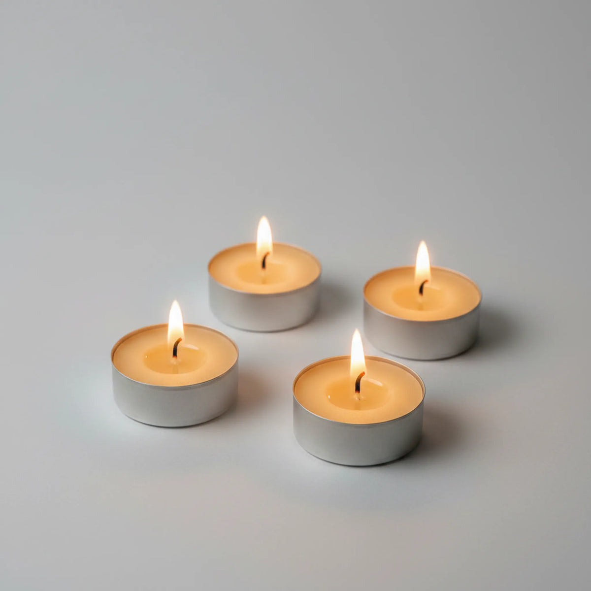 Four lit silver tea light candles arranged in a square on a clean light gray background.