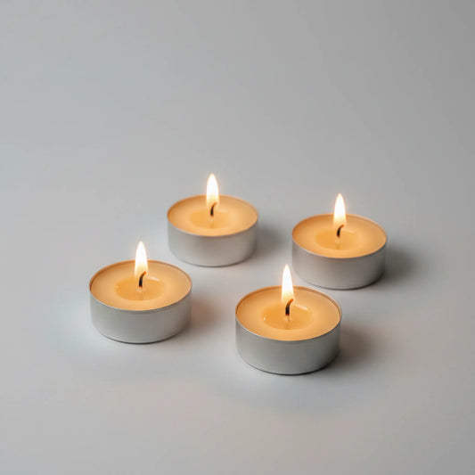 Four lit silver tea light candles arranged in a square on a clean light gray background.
