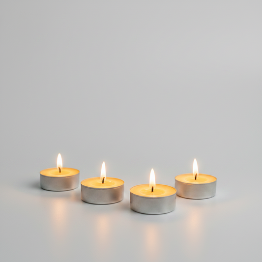 Four lit silver tea light candles arranged in a row on a light gray surface against a matching gray background.