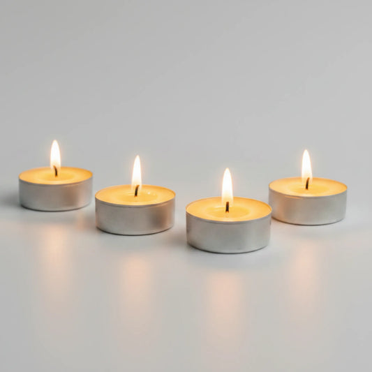 Four lit silver tea light candles arranged in a row on a light gray surface against a matching gray background.