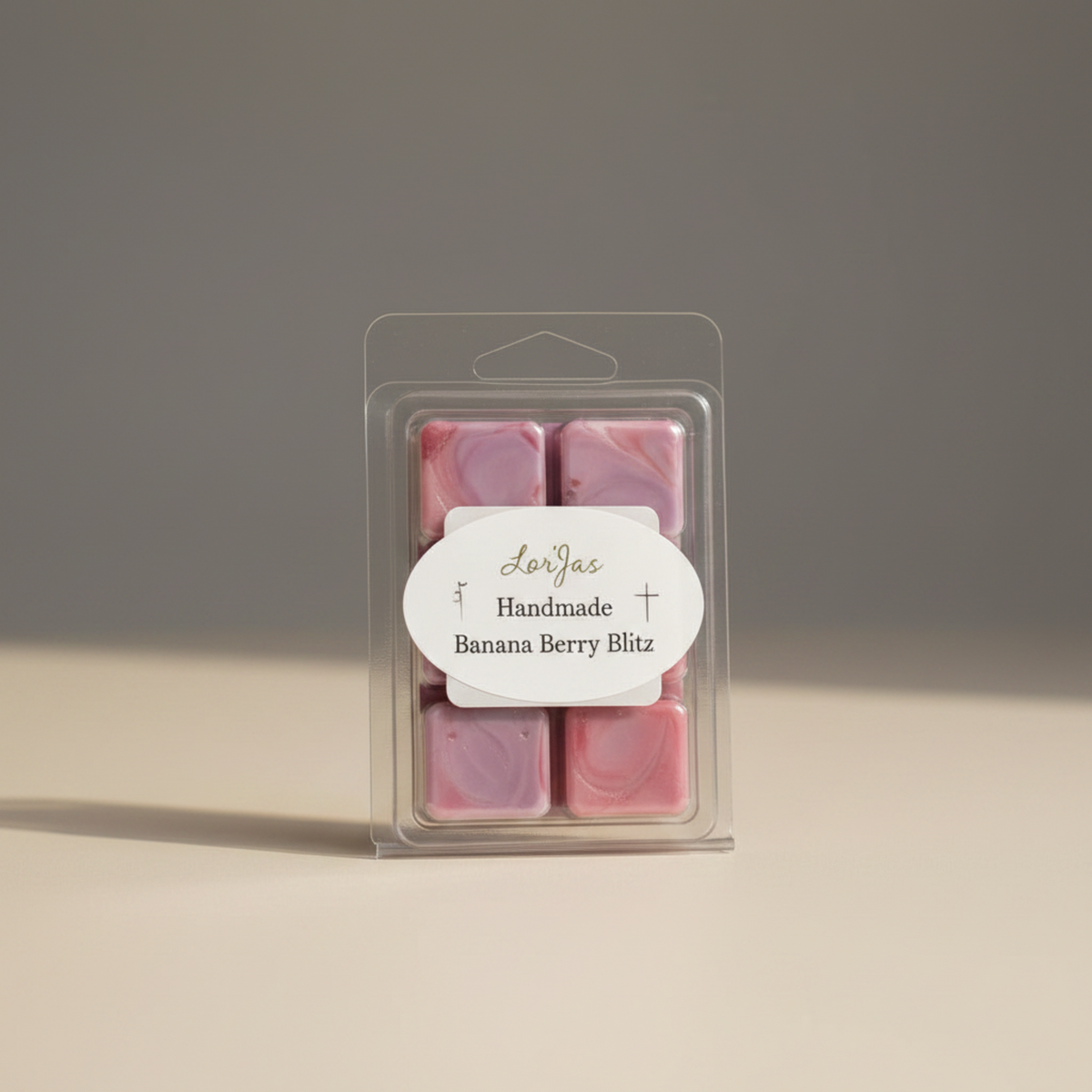 A clear clamshell package containing a lightly scented soy wax melts with a white oval label that reads 'LorJas Handmade Banana Berry Blitz' on a neutral beige and gray background.