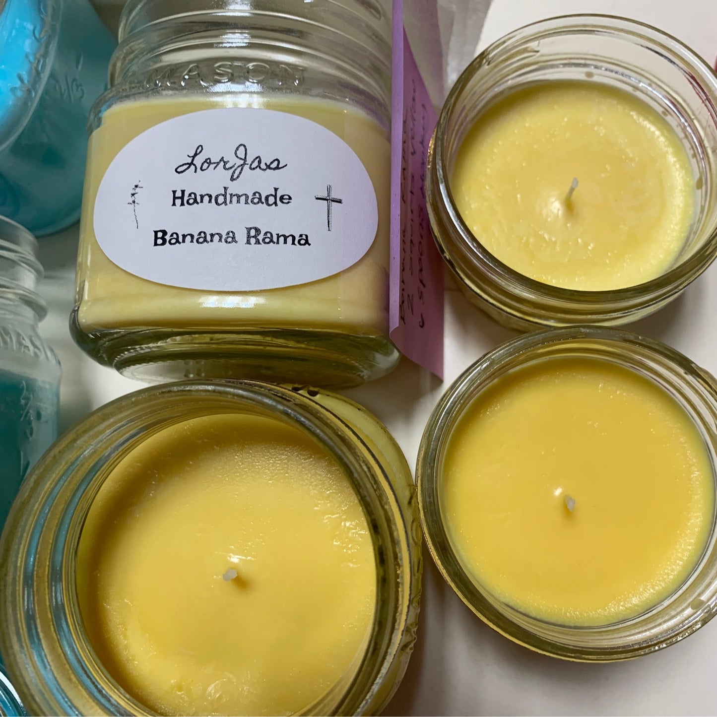 LorJas Handmade 'Banana Rama' candles in glass jars in various stages of processing with labels on a white surface.