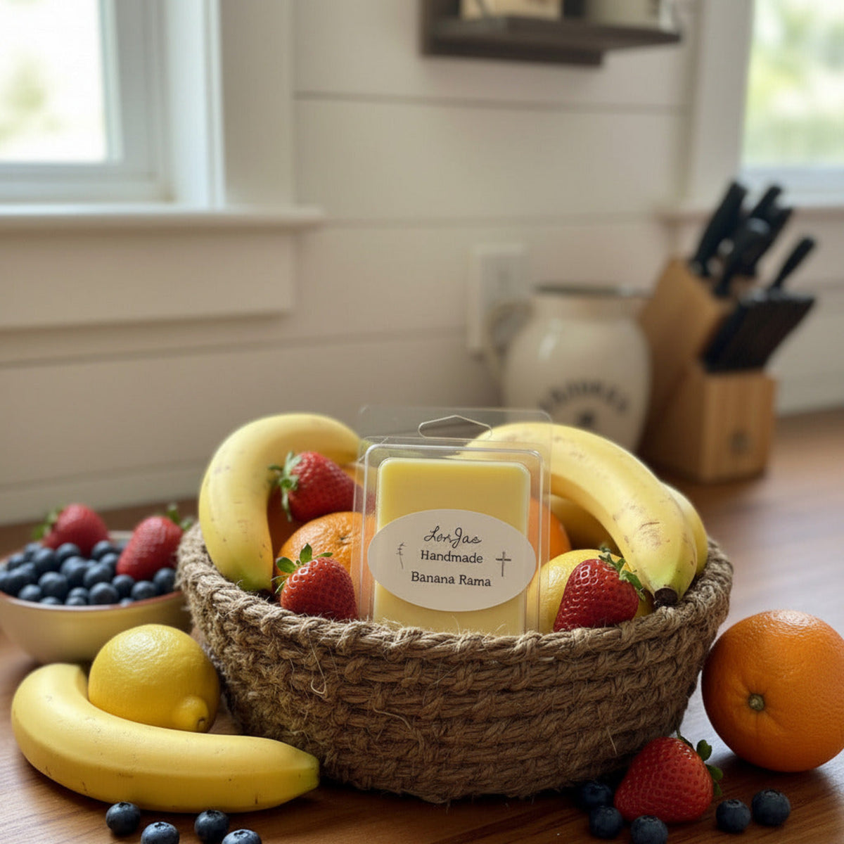 LorJas Handmade Banana Rama lightly scented soy wax melt in handmade rope basket of strawberries, oranges, lemons, and bananas with more fresh fruits including blueberries on a wooden kitchen counter.