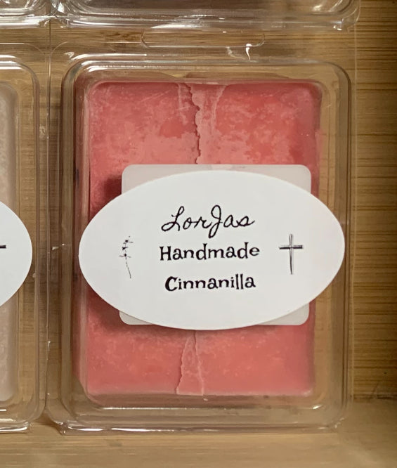 Pink wax melt in a clear container with a label reading 'Lorjas Handmade Cinnanilla' on a wooden surface.