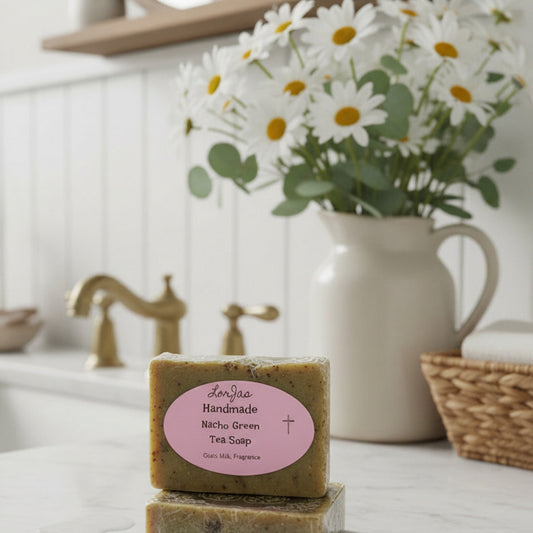Stack of LorJas Handmade Nacho Green Tea lightly scented goat milk soap on marble counter with a vase of daisies and a handwashing sink in bathroom setting.