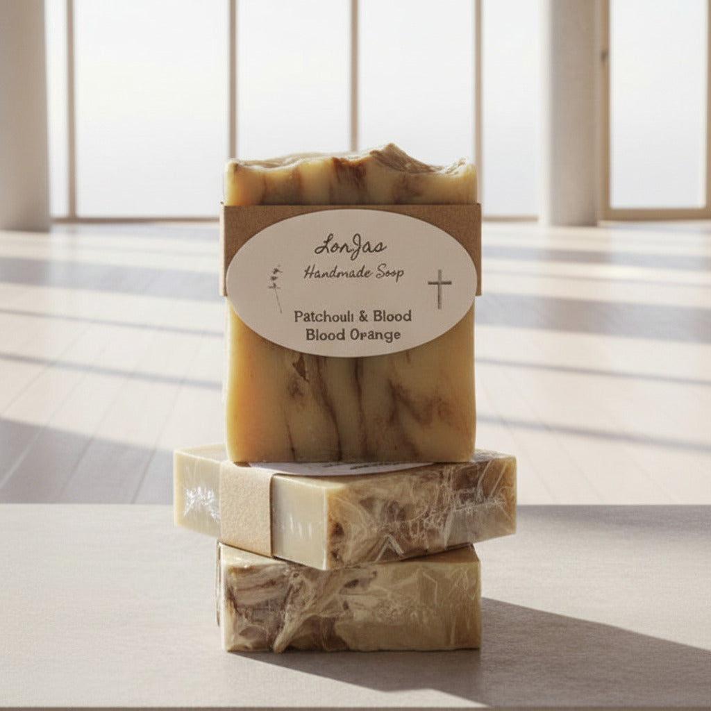 Three bars of LorJas Handmade Patchouli and Burnt Orange lightly scented Castile soap bars in a room with floor-to-ceiling glass windows flooding in natural light.