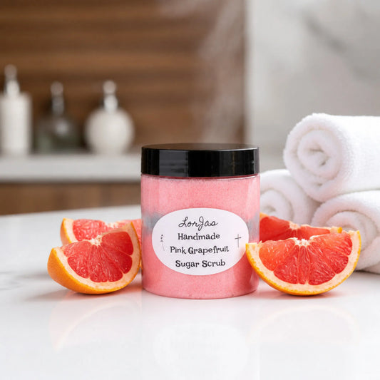 LorJas Handmade Pink Grapefruit lightly scented foamy whipped sugar scrub beside fresh-sliced pink grapefruit on counter beside rolled towels in steamy spa setting.