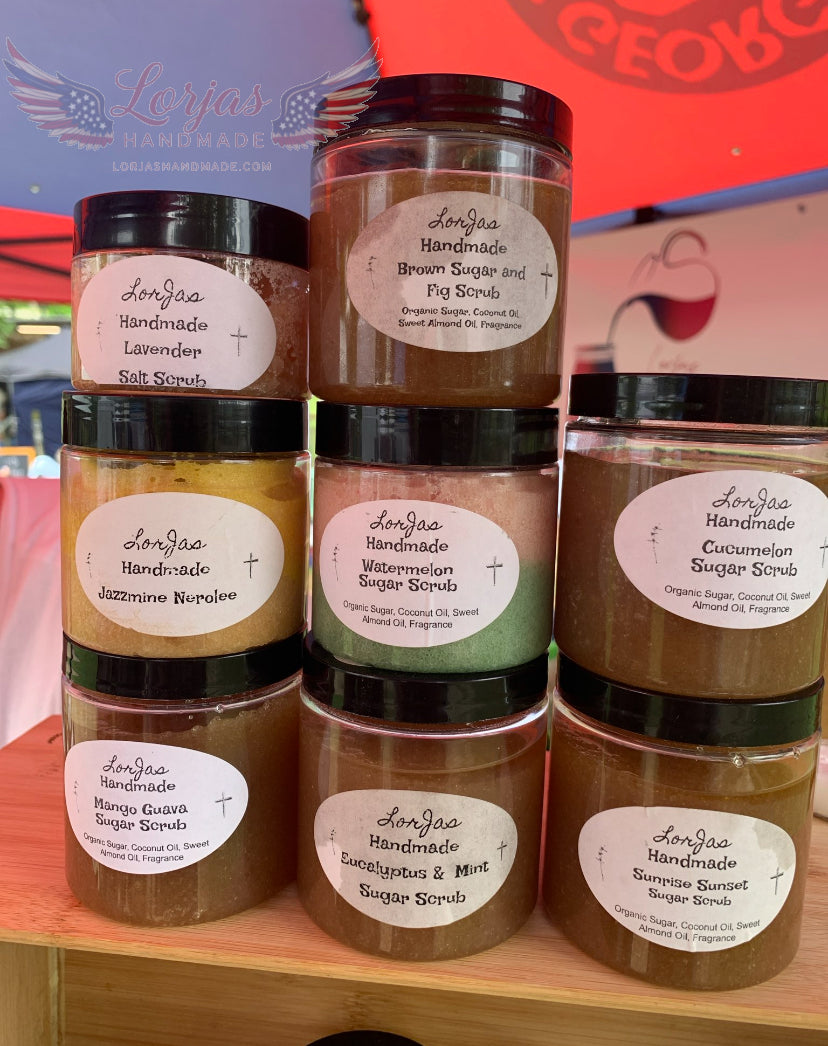 Collection of handmade sugar scrubs in jars with visible labels on a wooden shelf.