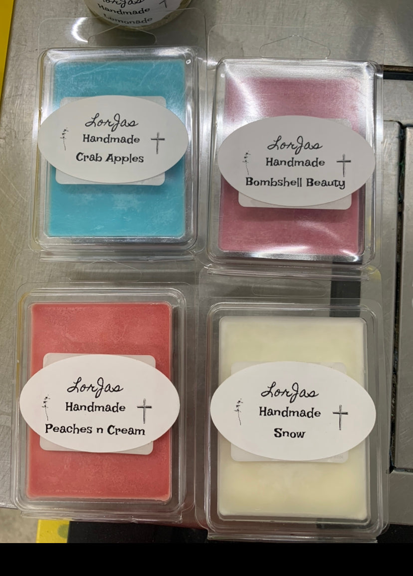 Four handmade wax melts in clear packaging with labels on a metal surface.