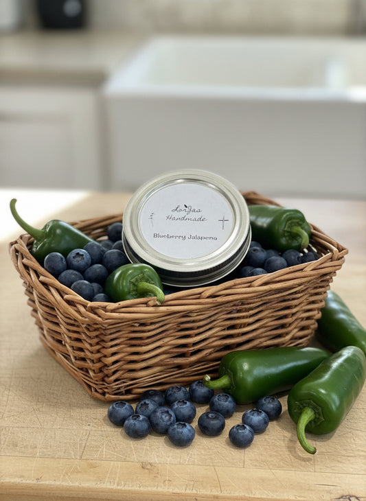 Jar of LorJas Handmade 'Blueberry Jalapeño' pepper jelly in basket of fresh blueberries and jalapeños.