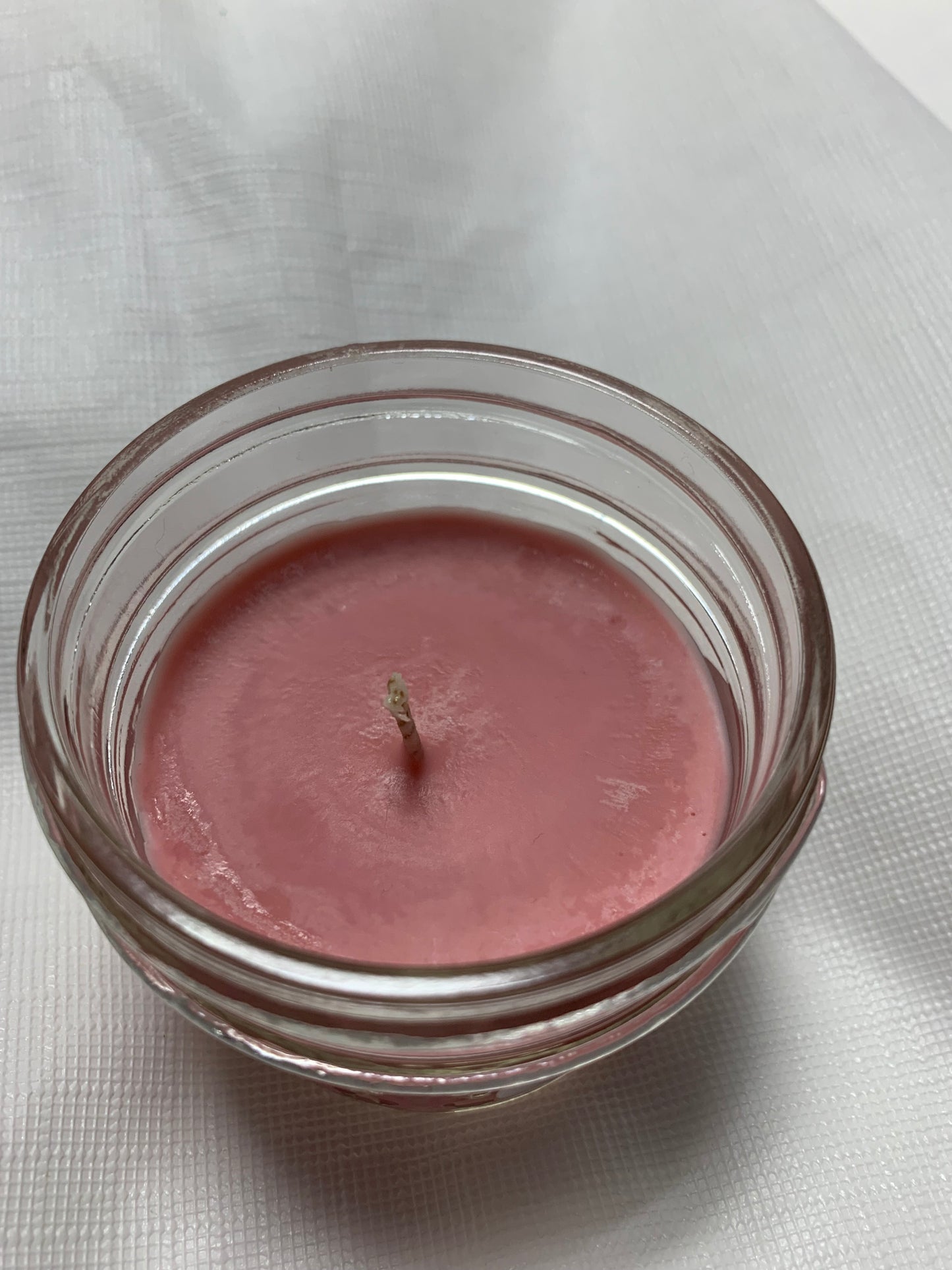 LorJas Handmade rose-colored organic scented soy wax candle in a clear glass jar on a white fabric background