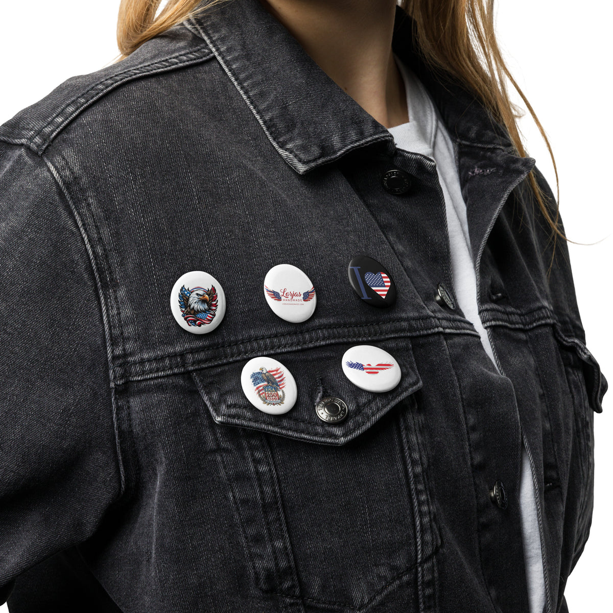 A close-up of a person wearing a dark washed denim jacket over a white shirt, featuring five patriotic-themed embroidered pins on the chest pocket.