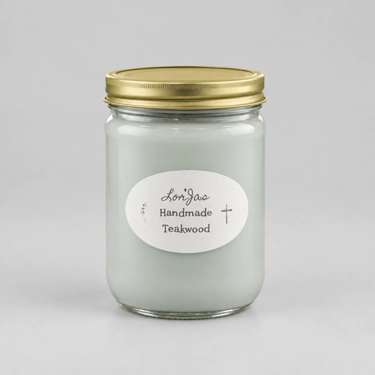 A glass jar candle with pale mint green wax, a gold metal lid, and a white oval label reading 'LorJas Handmade Teakwood' on a light gray background.