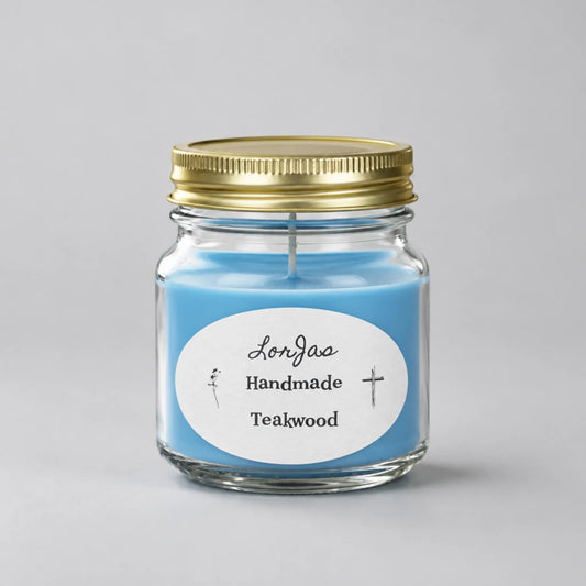 A blue scented candle in a clear glass jar with a gold metal lid and a white oval label reading 'LorJas Handmade Teakwood' on a light gray background.